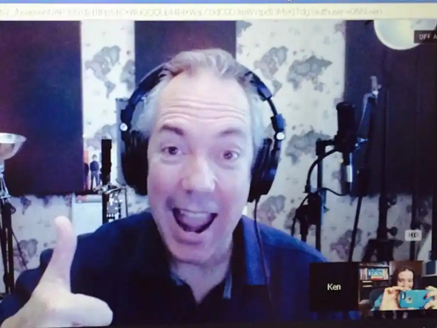 Ken Theriot wearing headphones gives a thumbs‑up and smiles enthusiastically during an online coaching session in his home recording studio.
