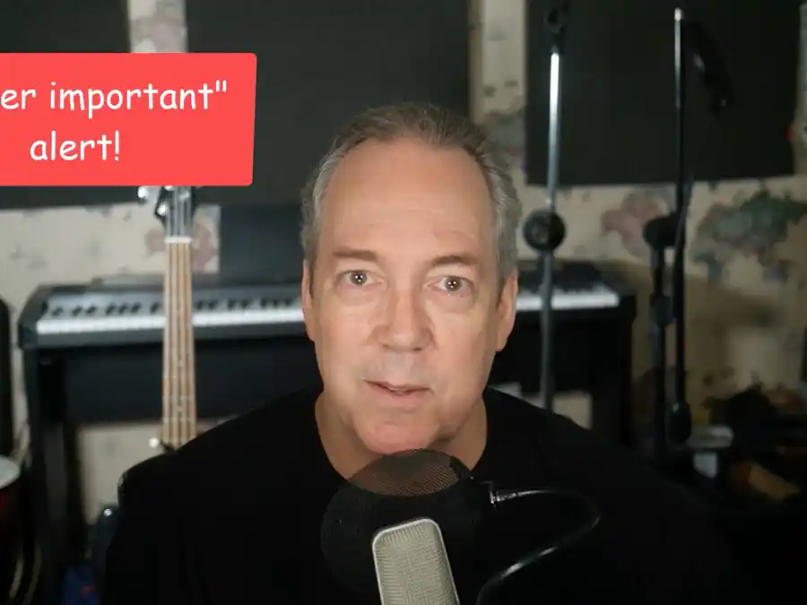 Ken Theriot talks into a studio microphone with a bass guitar and keyboard in the background, recording an online lesson.